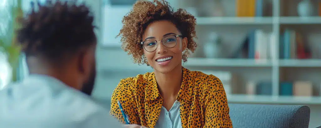 Smiling woman psychologist wearing glasses and a leopard print top sits across from someone in an office setting.