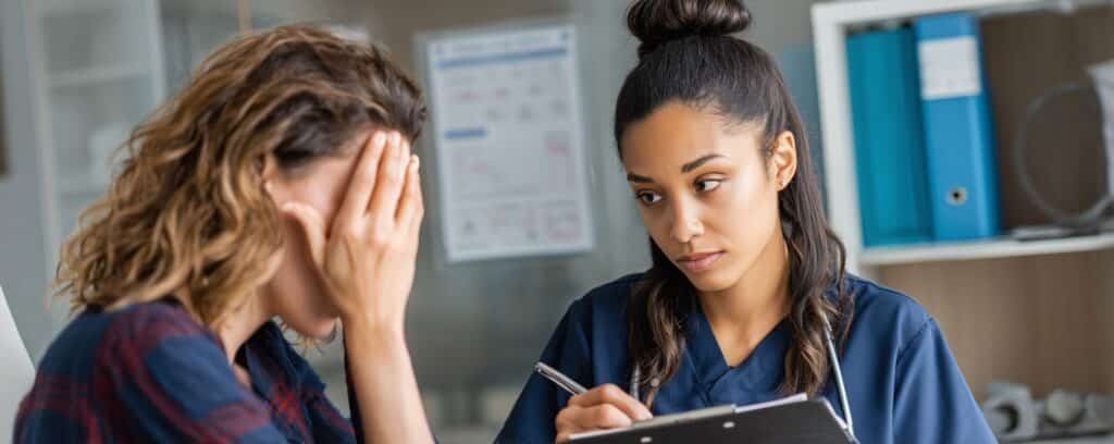 A nurse listens attentively to a distressed woman covering her face during a consultation.
